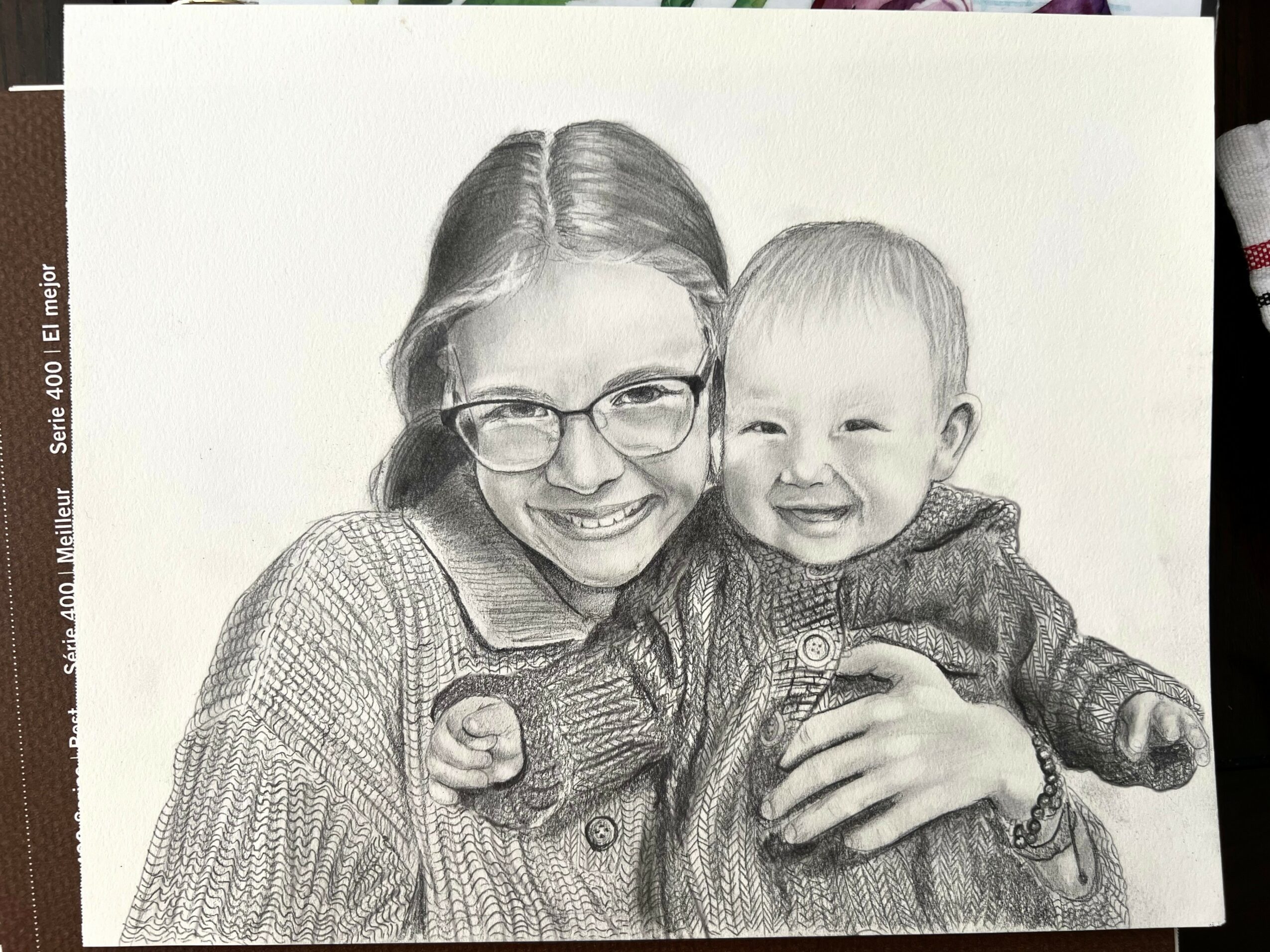 A woman with glasses and a young child are smiling and hugging each other, in a black-and-white sketch style.