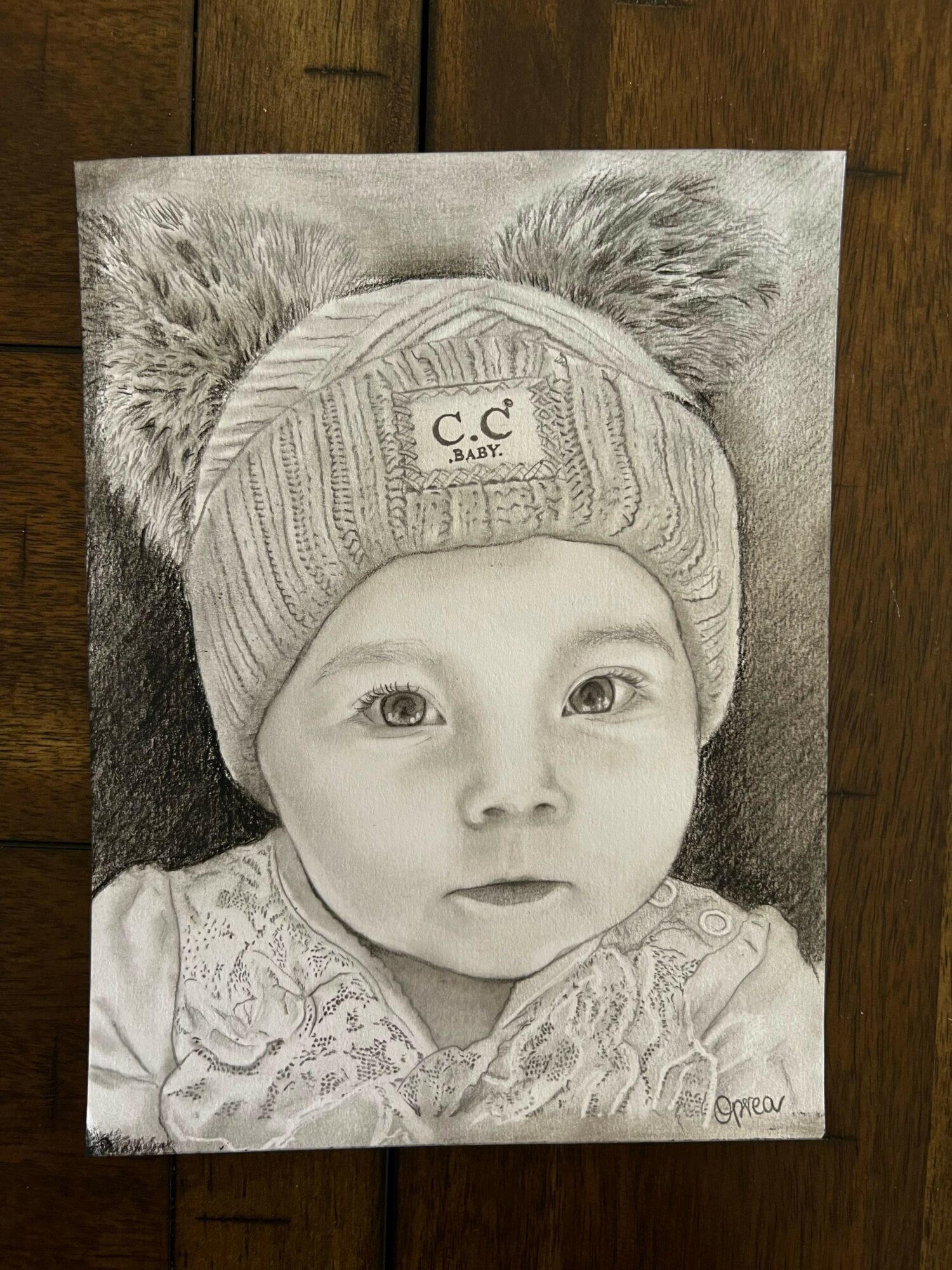 Pencil sketch of a young child wearing a beanie, lying on a furry surface, with detailed facial features and clothing.