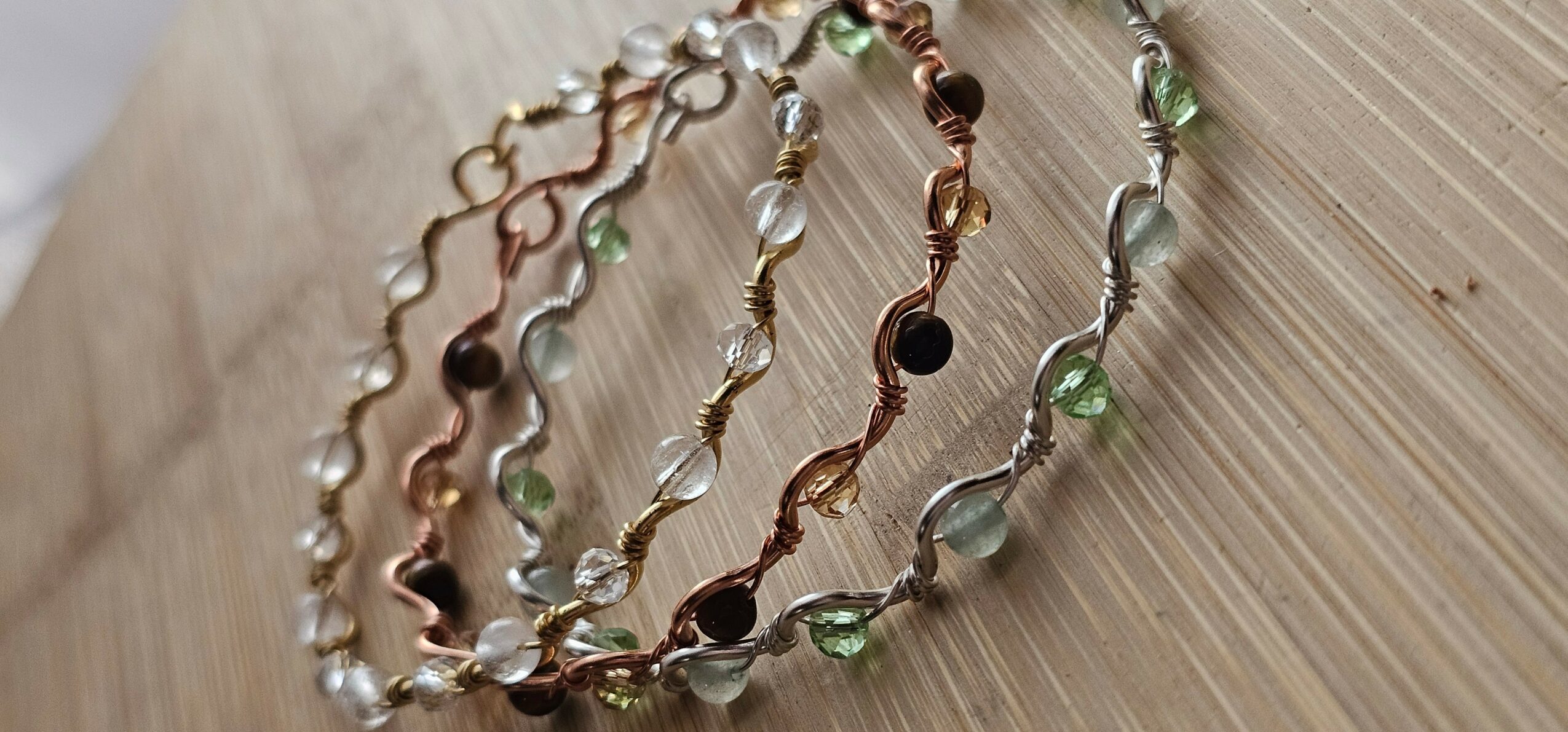 Four necklaces with beads and metal links, arranged on a wooden surface.