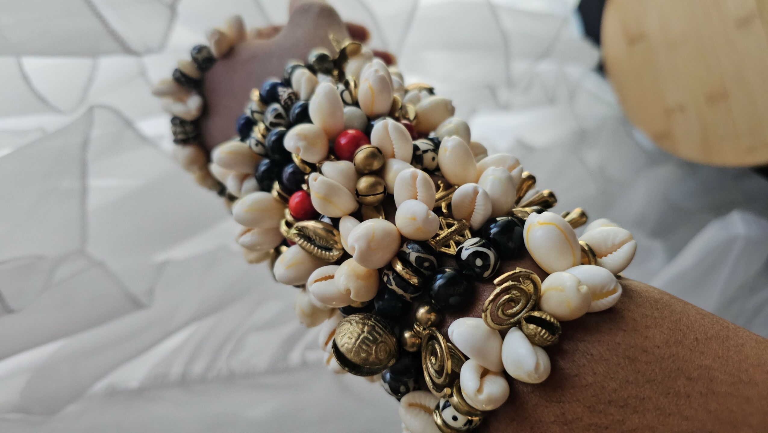 Multiple beaded bracelets with white, black, and gold beads on a person's wrist, against a blurred background.