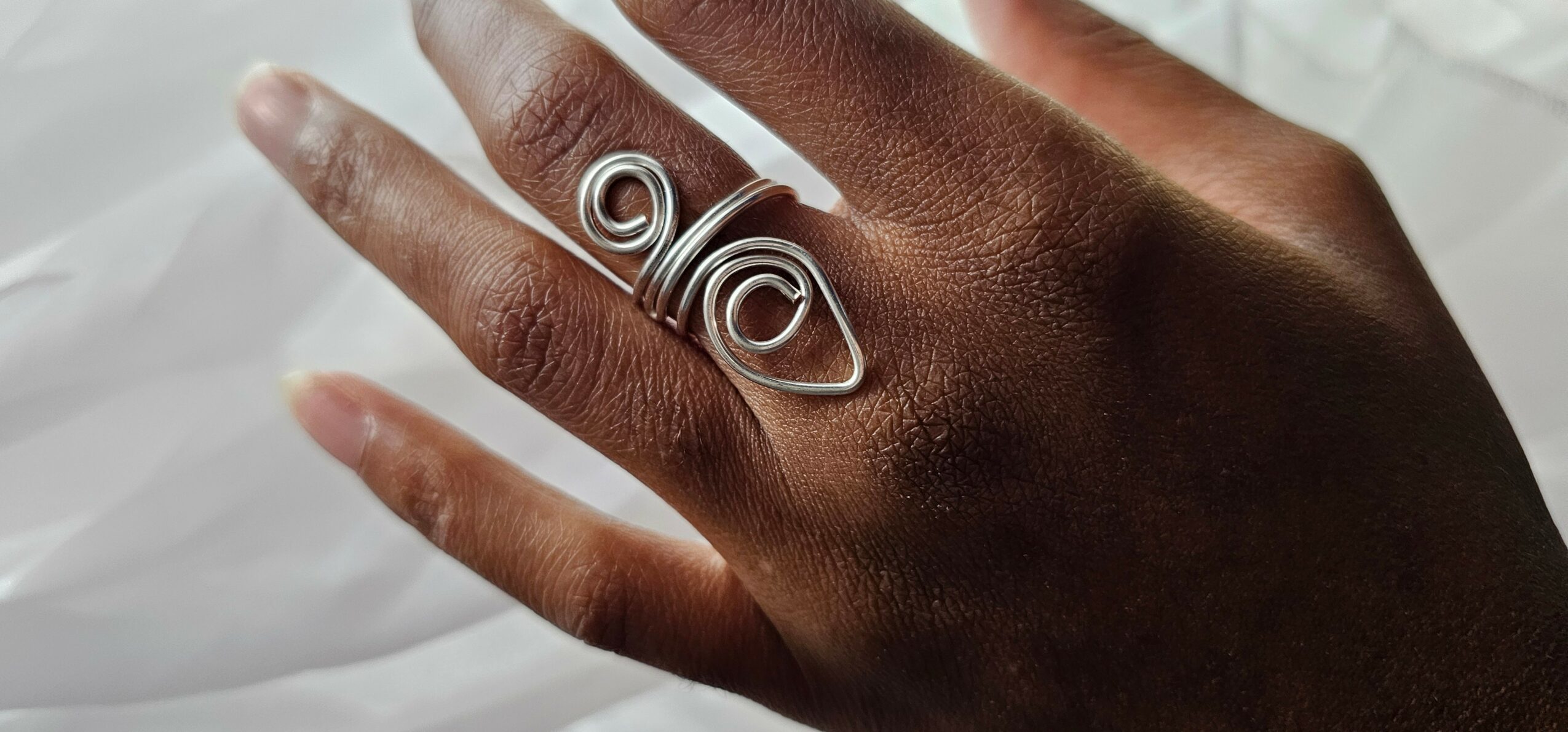 Hand with a silver wire ring on the middle finger, against a light background.