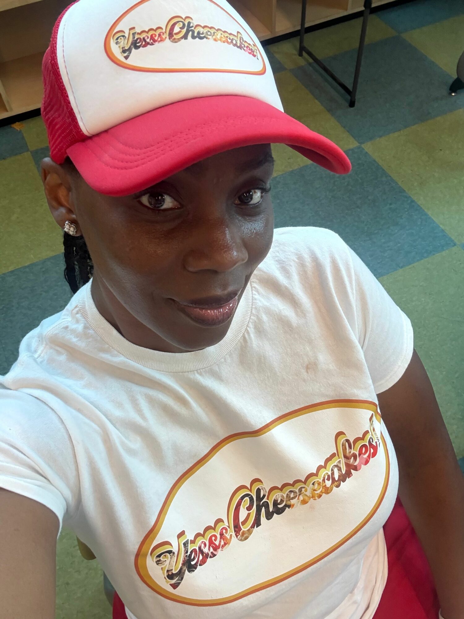 Person wearing a white t-shirt and a red and white cap, looking at the camera, indoors.