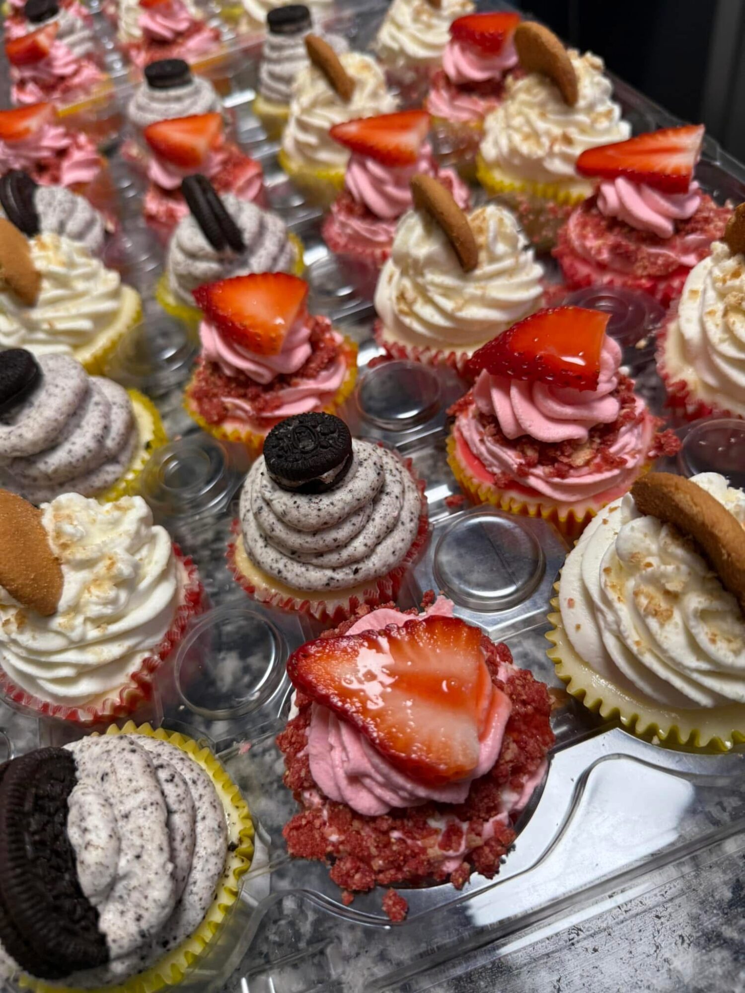 Assorted cupcakes with various toppings including strawberries, cookies, and cream, arranged on a tray.