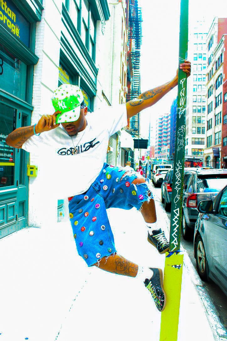 Person jumping on city street, wearing a white shirt, blue shorts with red dots, and a green hat, holding a pole.