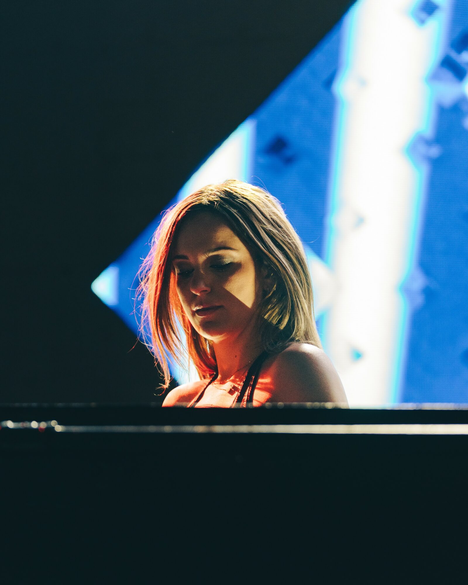 A woman with shoulder-length hair looks downward, illuminated by blue and white lights in the background.