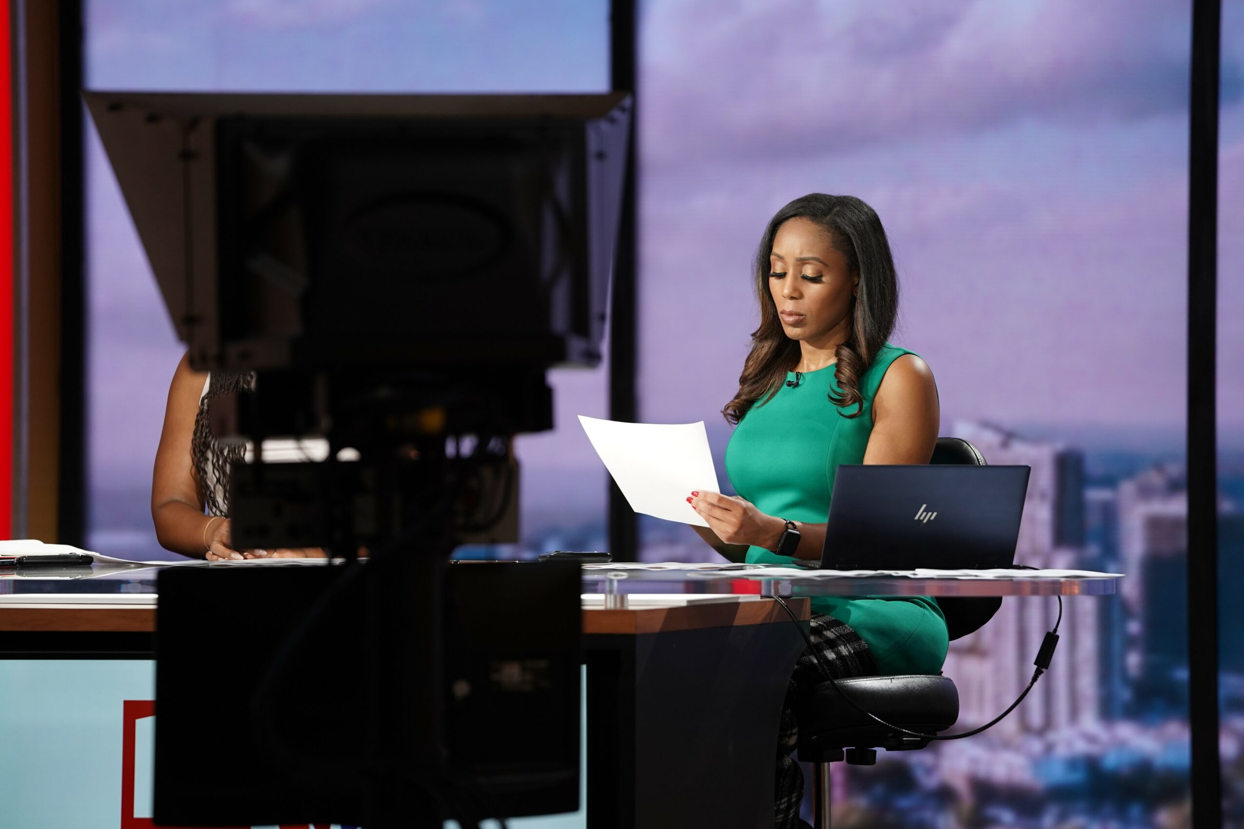Woman in green dress reading paper at desk with city view background.