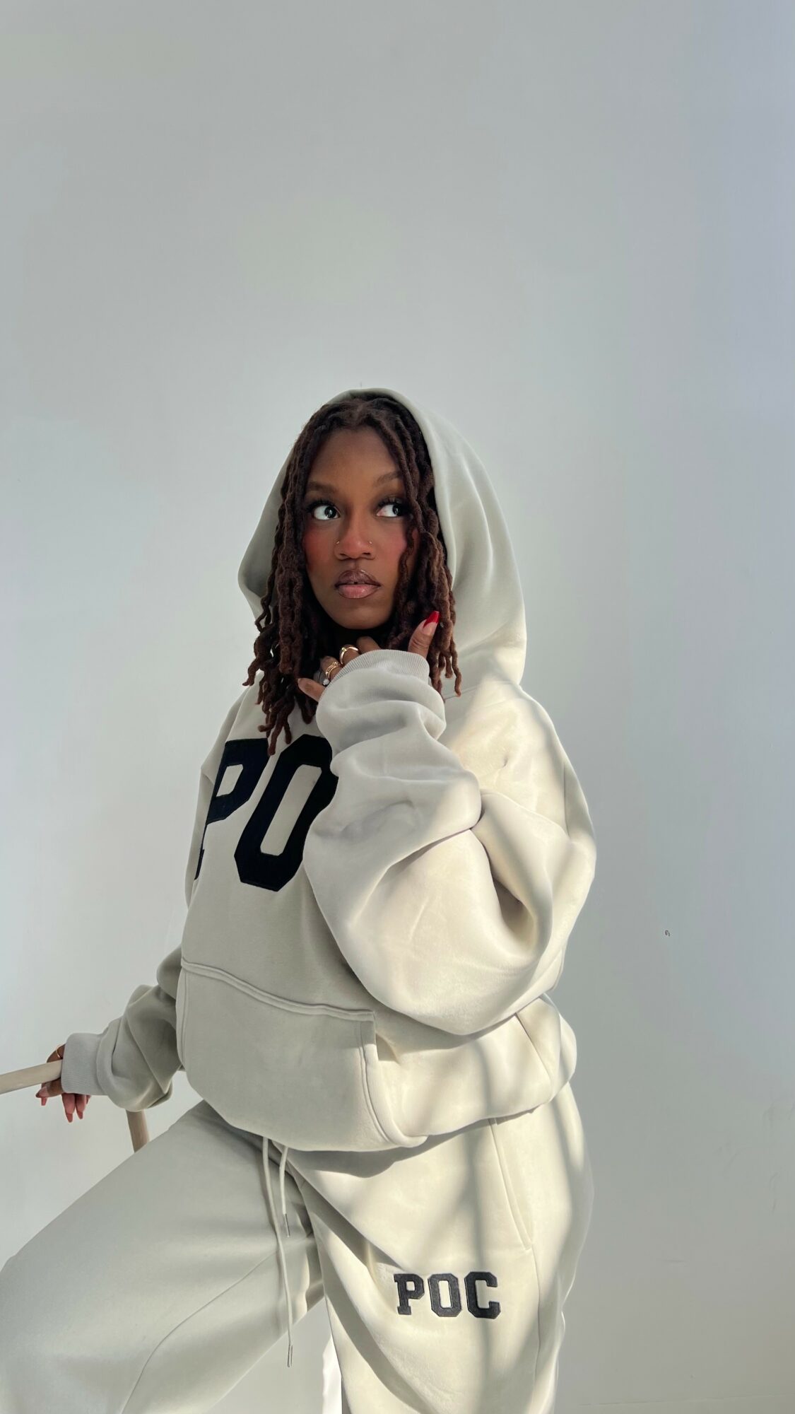 Young woman with braided hair wearing a hoodie and sweatpants, looking to the side against a plain background.