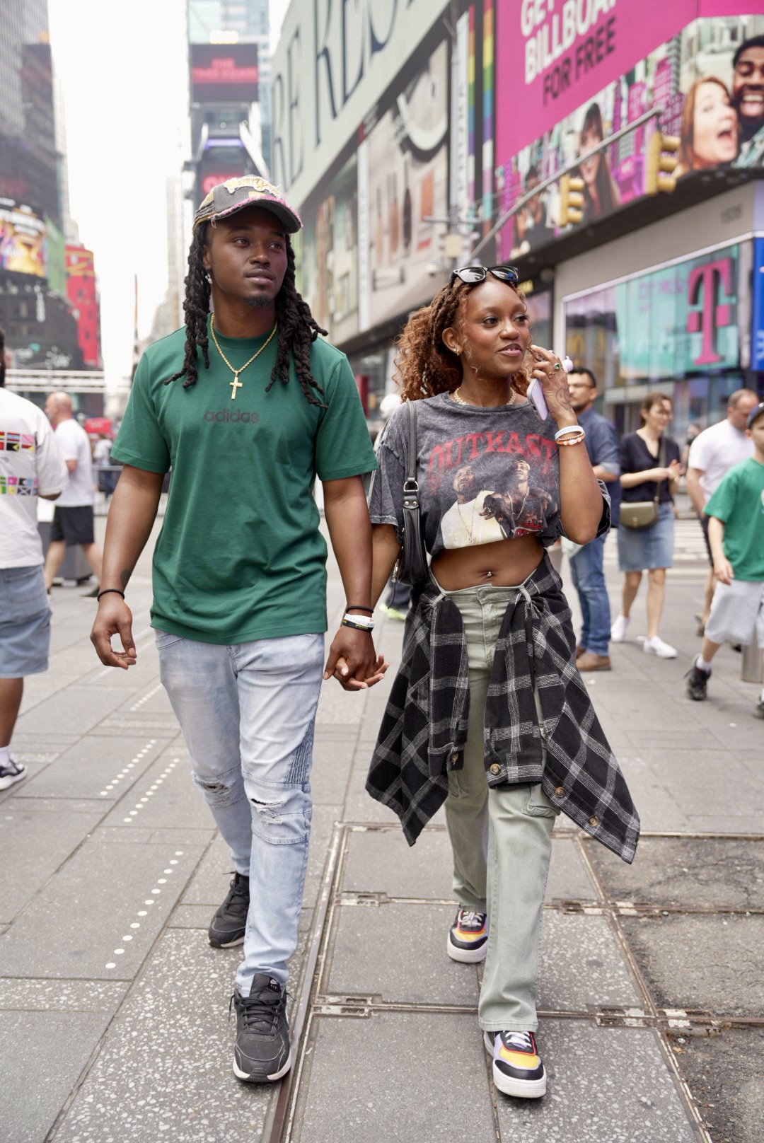 Two young people walking on a busy city street with billboards and crowds around them.