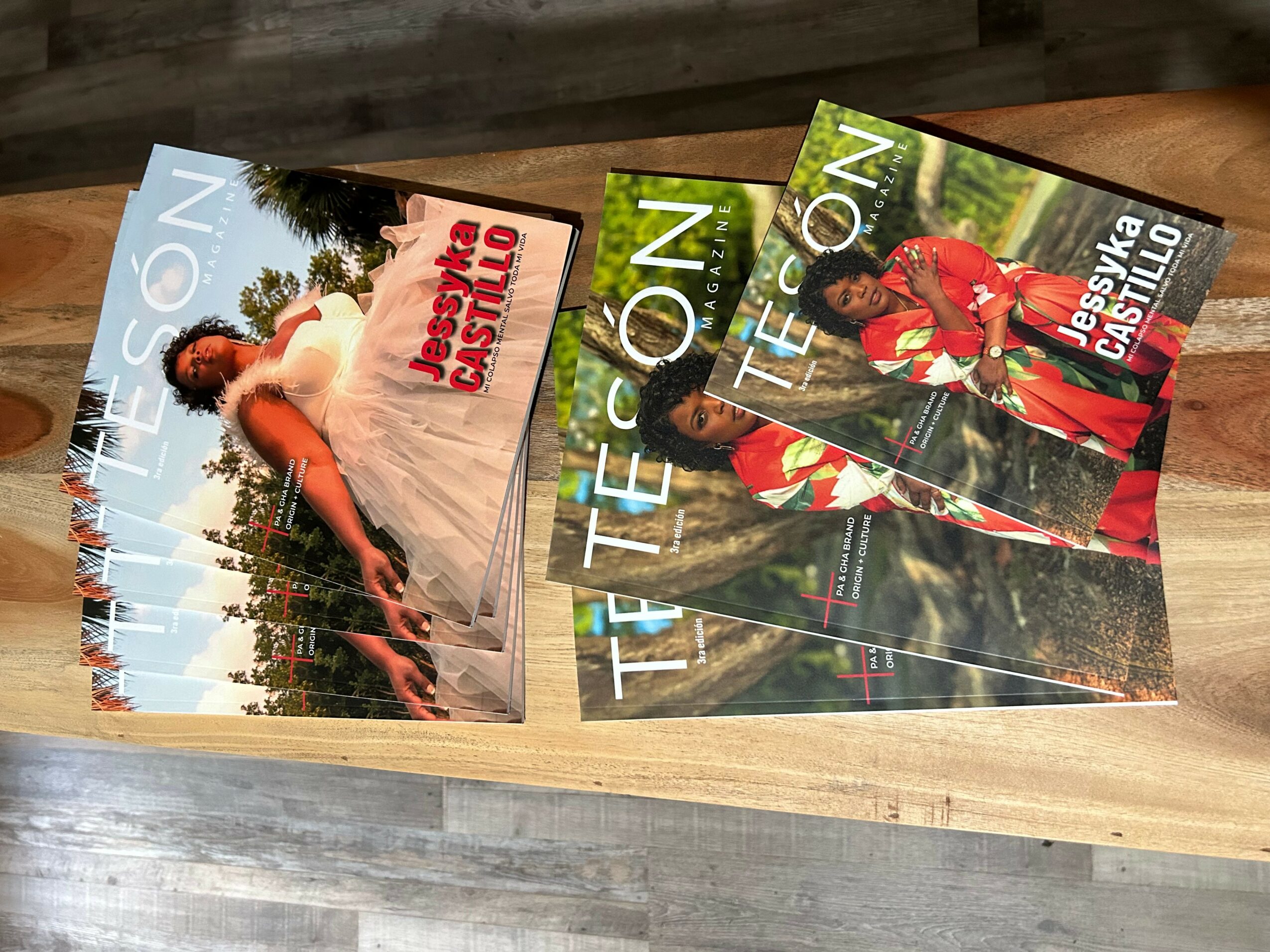 Three magazines with colorful covers, one featuring a woman in a white dress outdoors, others with people in costumes, on a wooden surface.
