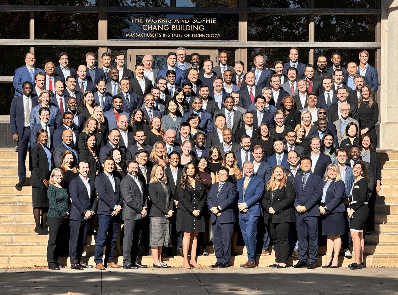 Large group of professionally dressed people standing on steps outside a building, posing for a photo.