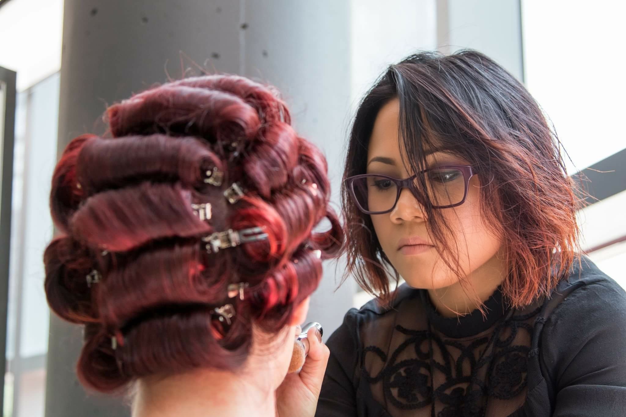 Woman with glasses and shoulder-length hair looks at a person with red curled hair, indoors near a window.