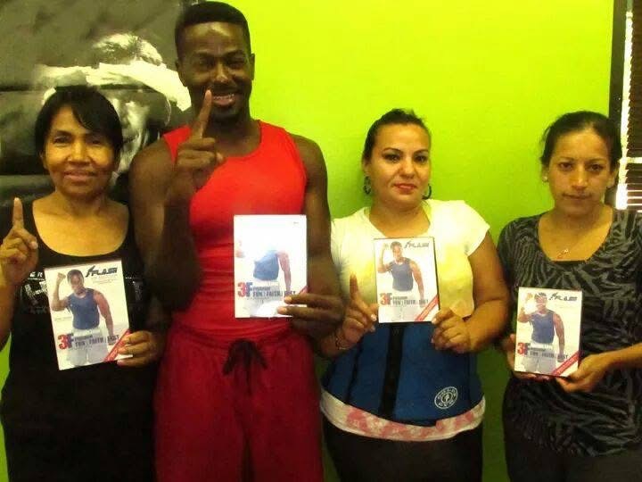 Four people holding certificates, standing against a green wall, smiling, with one person in a red outfit, others in casual clothing.