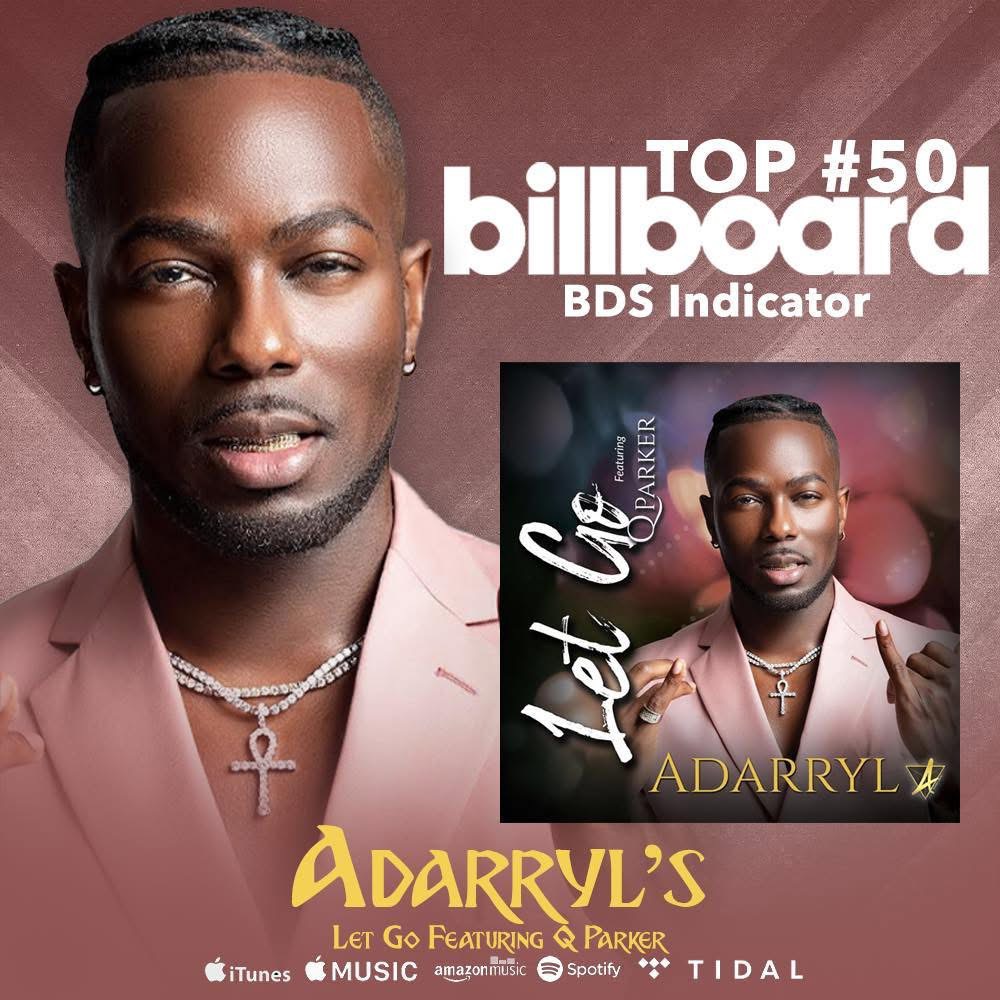 Close-up of a man with braided hair, wearing a pink blazer and jewelry, against a pink background.