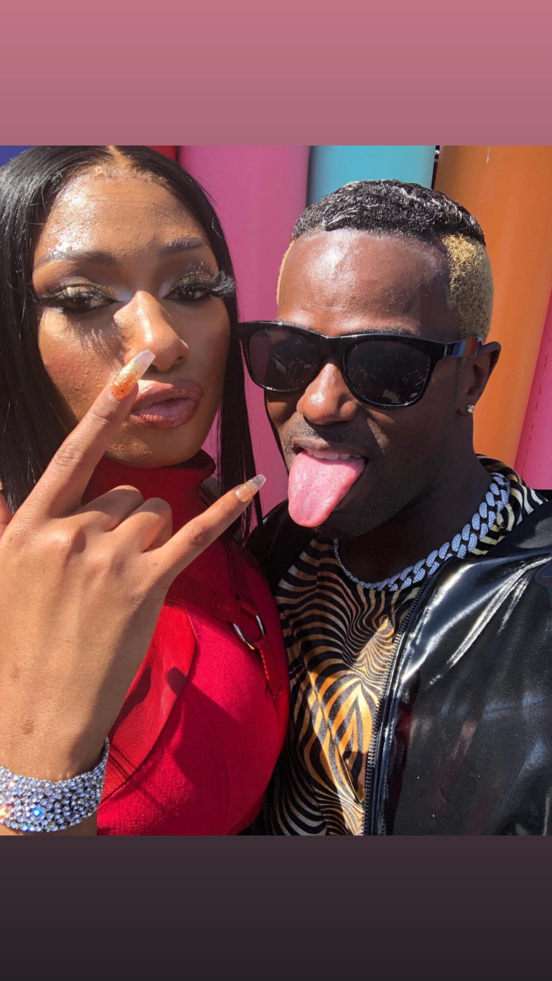 Two people posing for a selfie, one with long dark hair and makeup, the other with sunglasses and sticking out tongue.