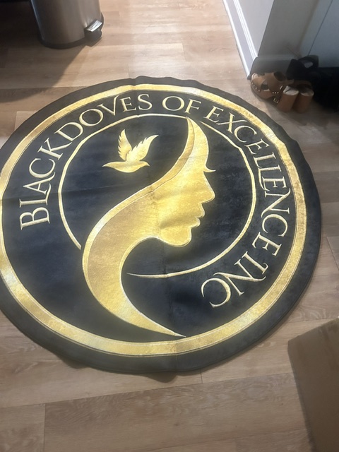 Round black and gold sign with a stylized bird and the text 'Black Voices of Excellence Inc'.
