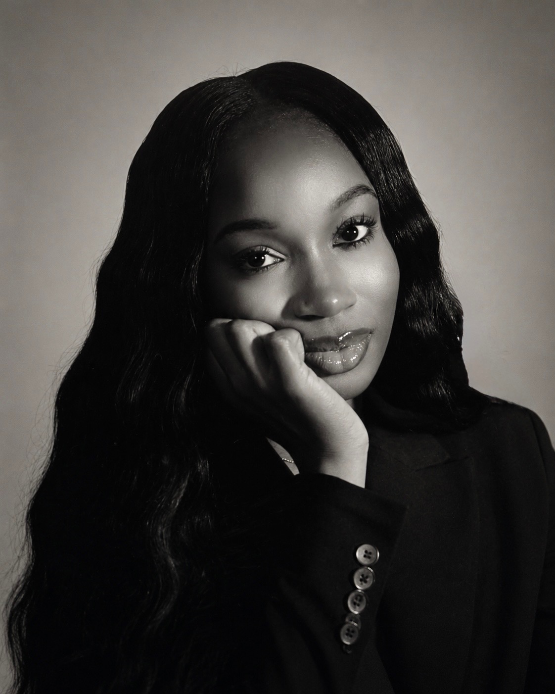 Portrait of a woman with long wavy hair, resting her chin on her hand, looking at the camera, in black and white.
