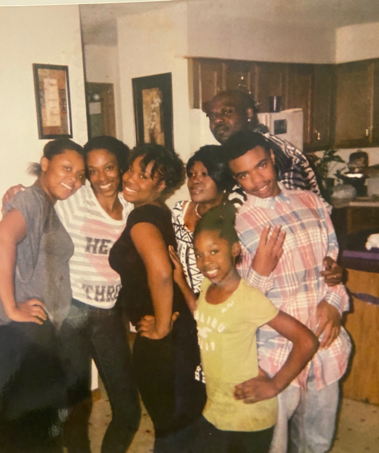 Group of six people smiling and posing indoors, with a kitchen in the background.