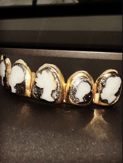 Five gold-wrapped chocolates with white and dark filling, arranged in a row on a dark surface.