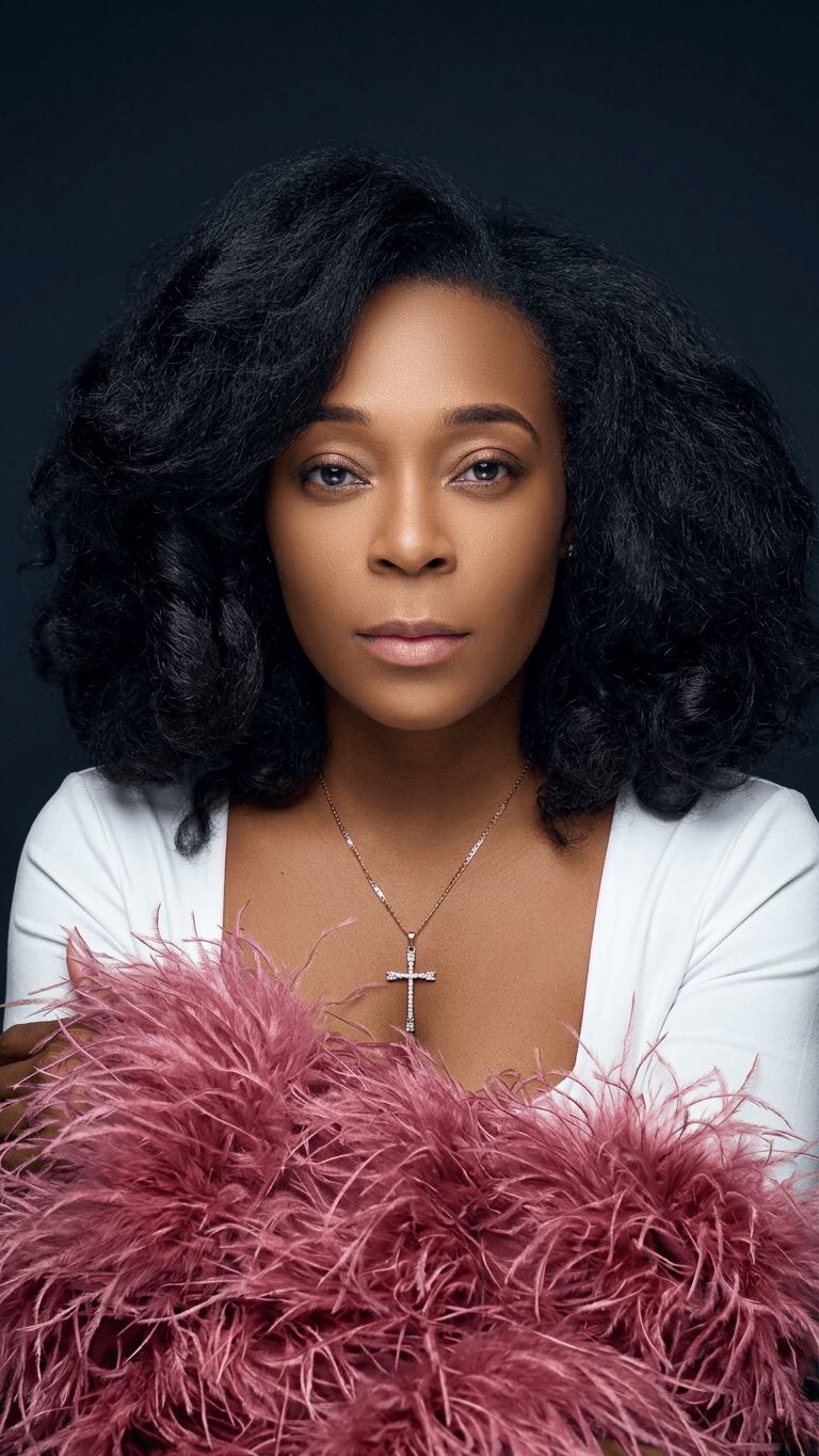 Portrait of a woman with curly black hair, wearing a white top and a cross necklace, holding pink feathers.