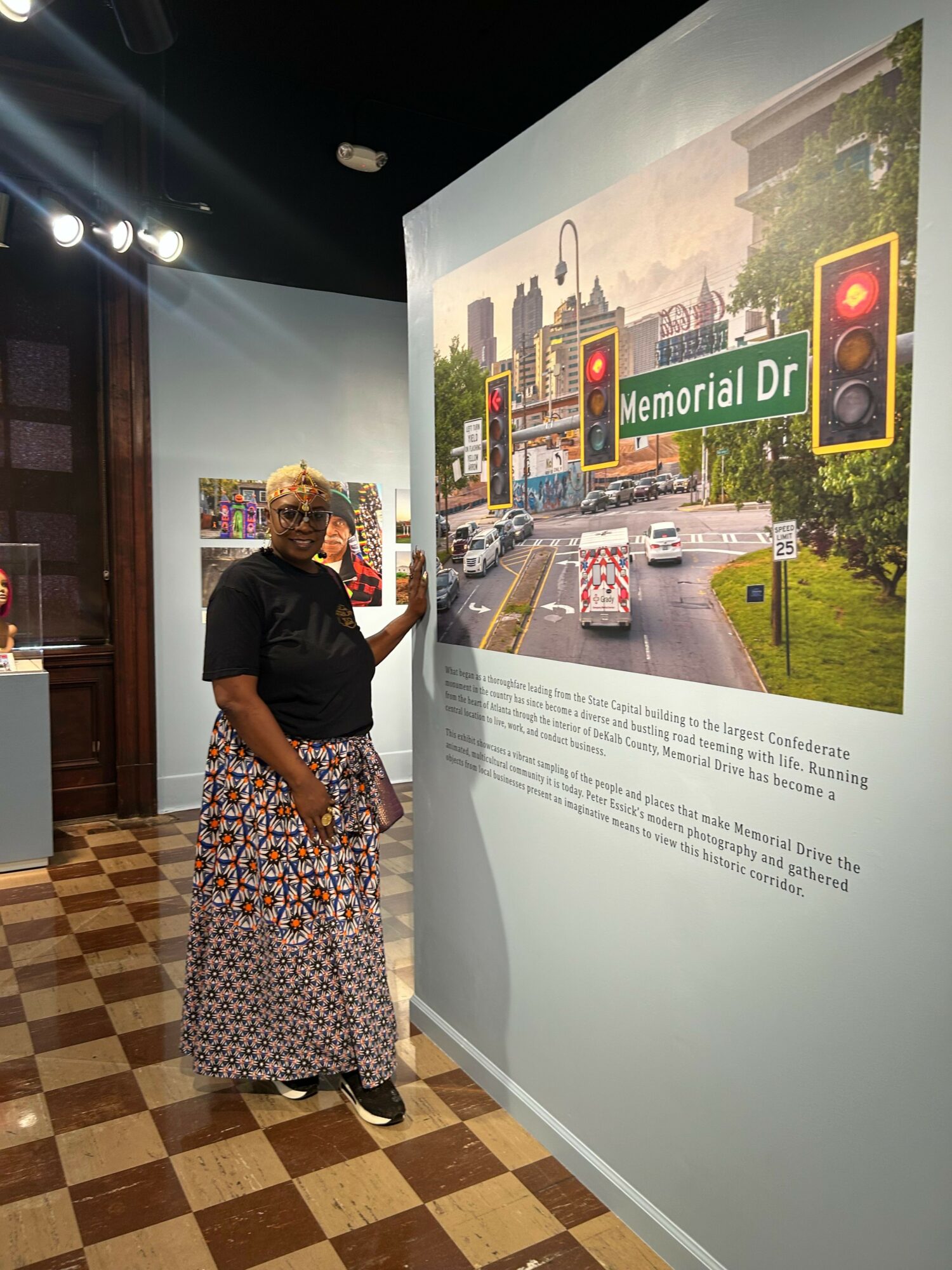 Woman looking at an informational display about a street with traffic lights and buildings, standing on a checkered floor.