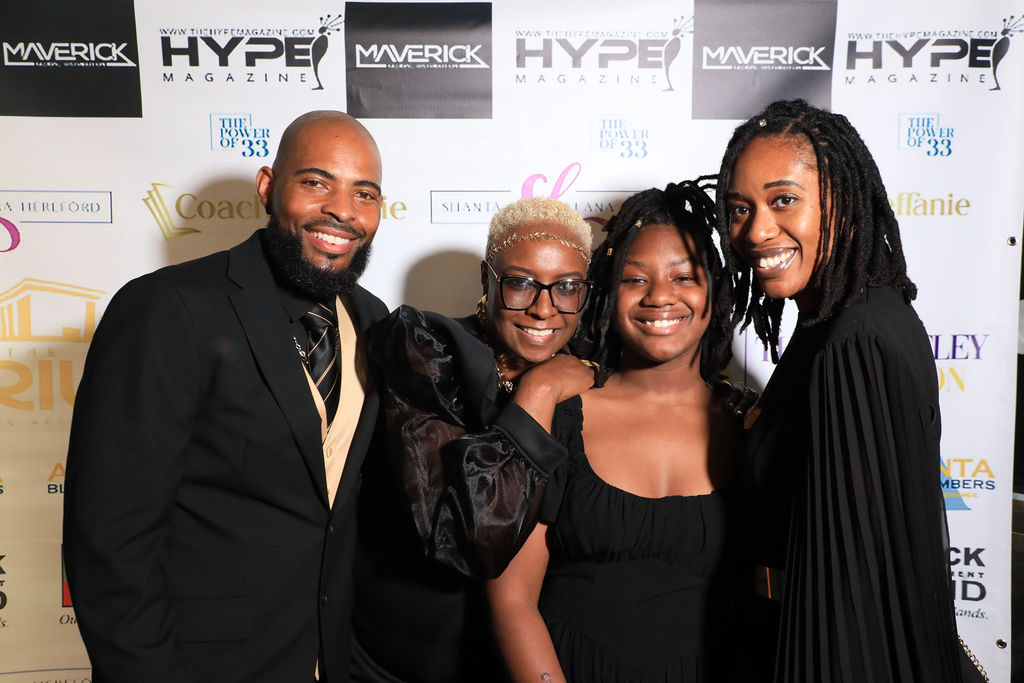 Four smiling people standing together in front of a backdrop with logos, posing for a photo.