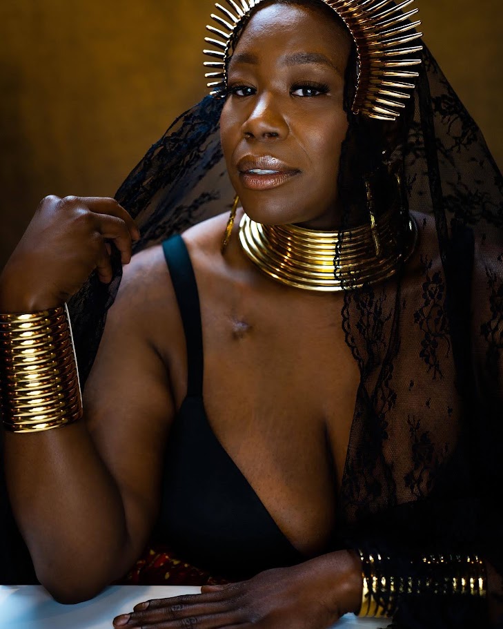 Woman with gold jewelry, black lace veil, and dark clothing, looking confidently at the camera.