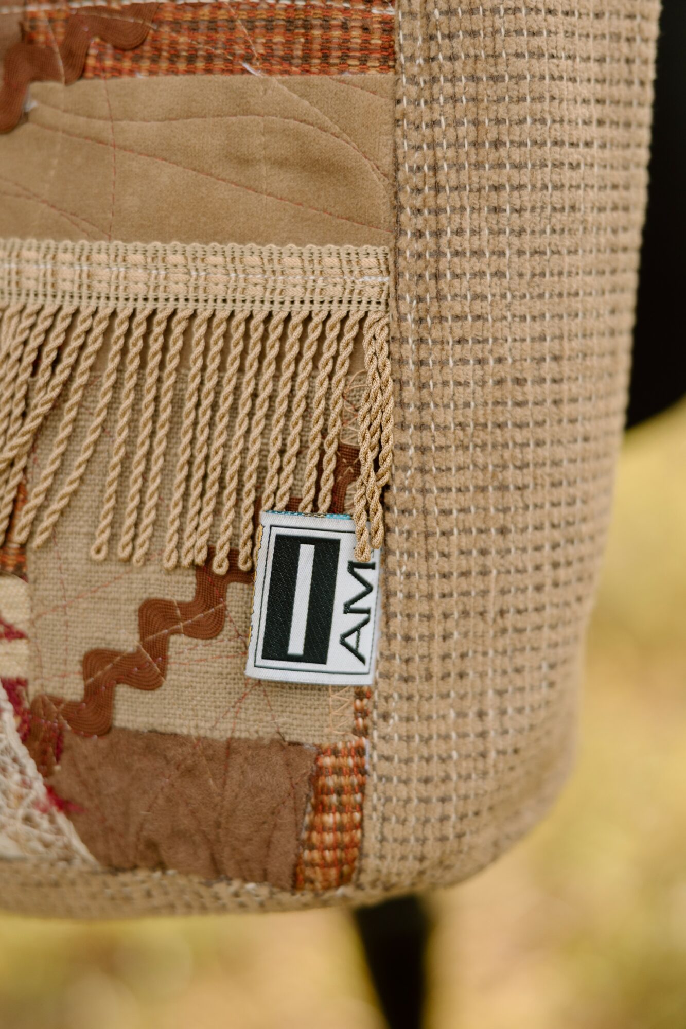 Close-up of a fabric bag with fringe, camouflage pattern, and a tag, showing textured materials and stitching.