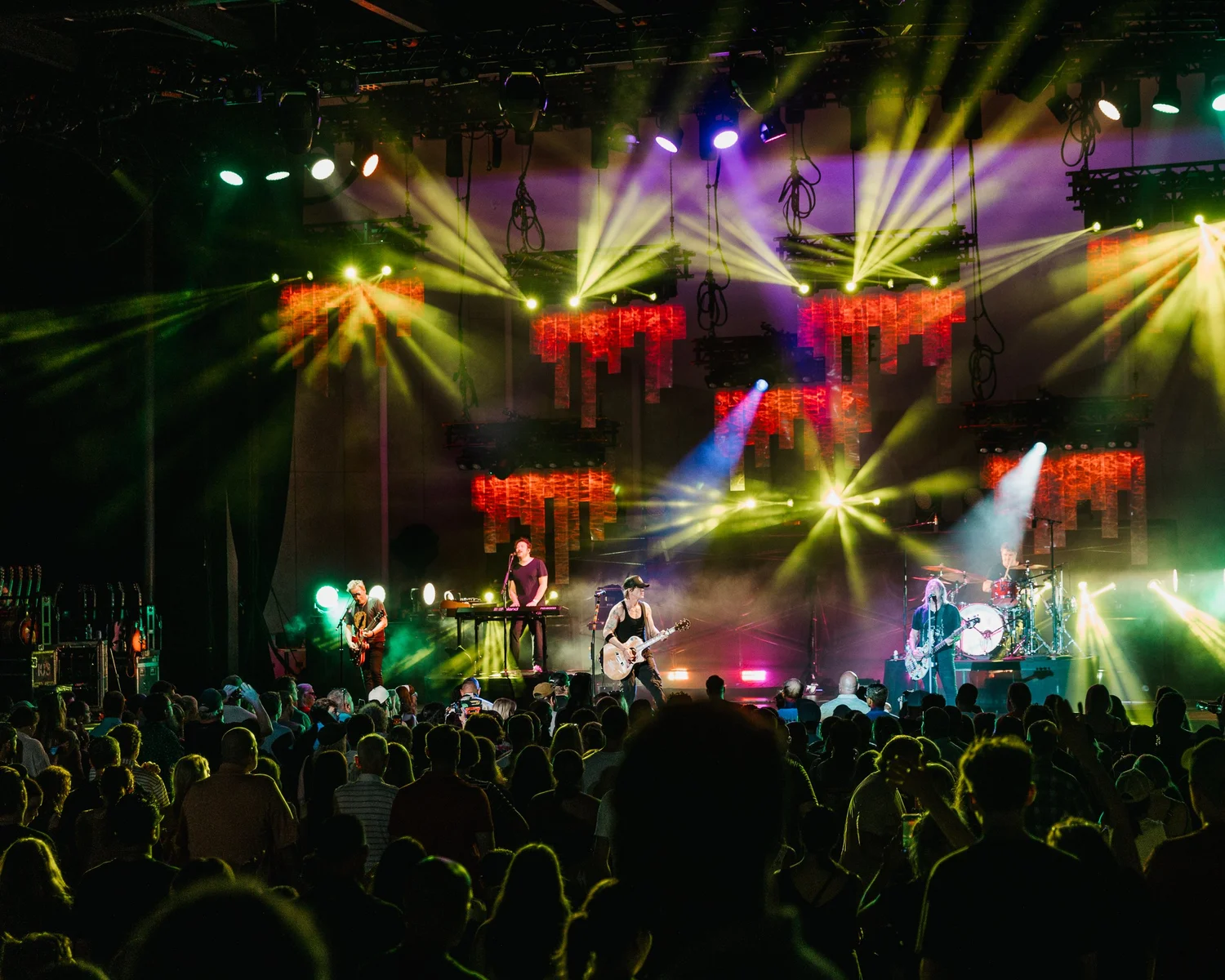 Concert stage with musicians and colorful stage lights, audience in foreground, vibrant atmosphere.