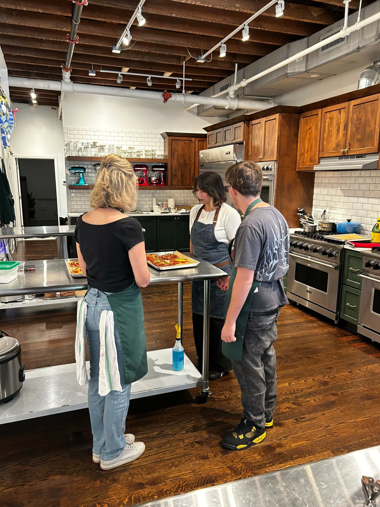 Three people in a kitchen, two men and one woman, preparing food on a wooden countertop.