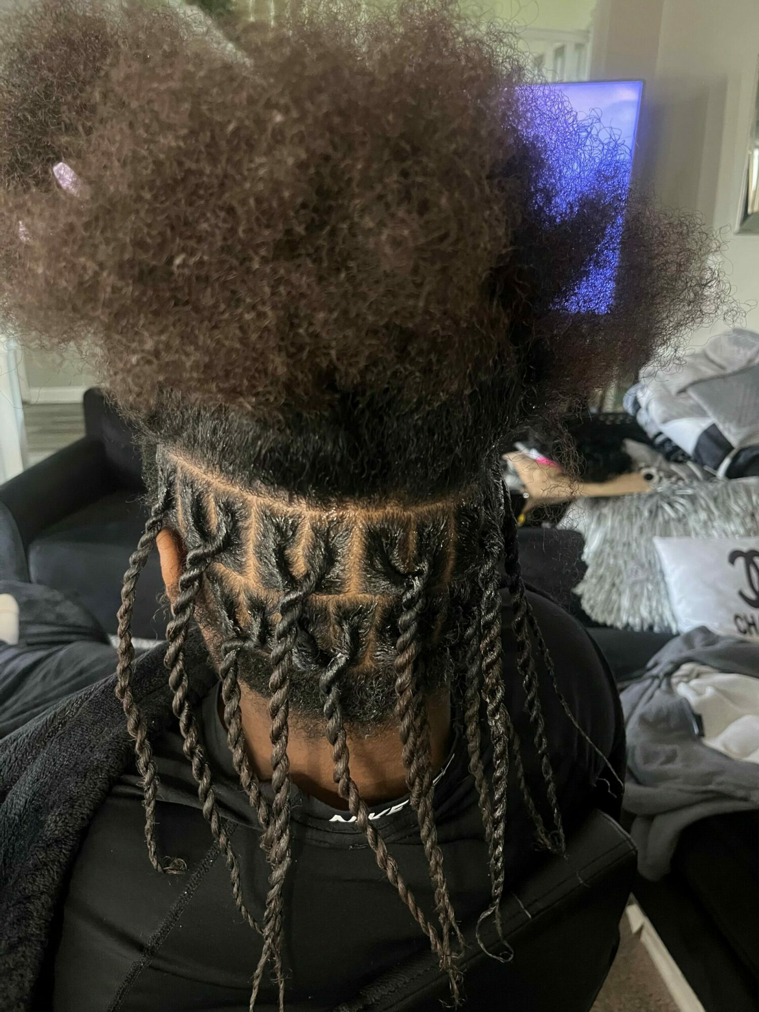 Person with braided hairstyle and natural hair, sitting in a room with a TV in the background.
