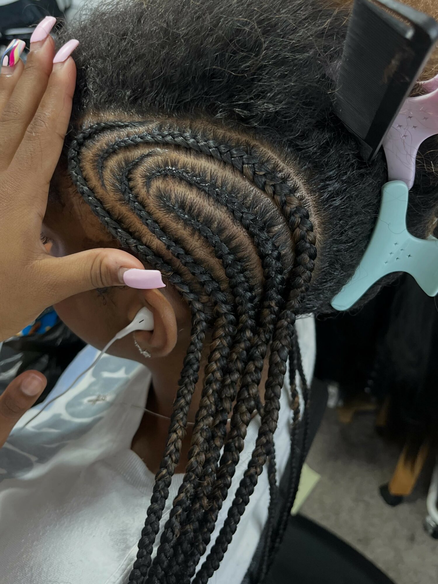Person with braided hair styled in a spiral pattern, secured with a hair clip, and a hand with pink nails touching the hair.