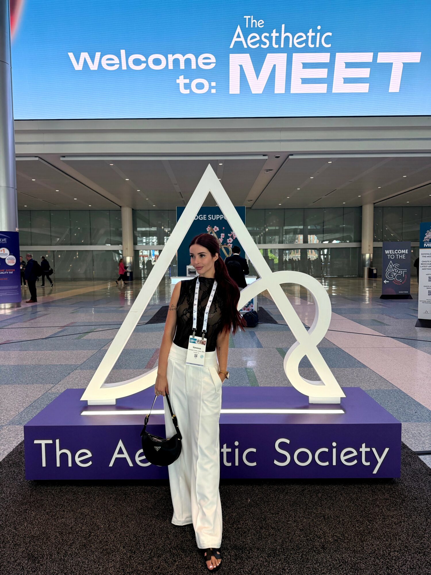 Woman standing in front of a large geometric sculpture at an event entrance, with a sign reading 'The Aesthetic Society'.
