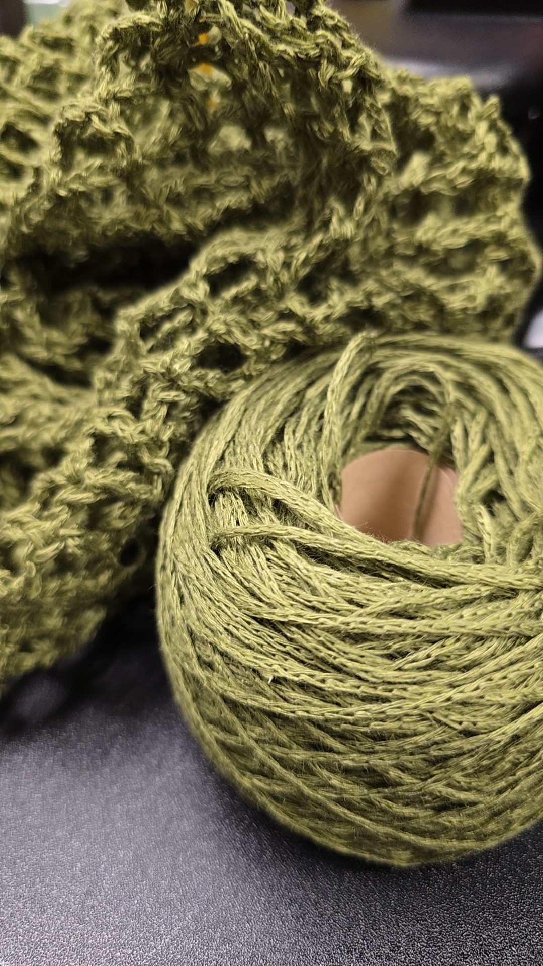Close-up of a ball of green yarn and a textured green sponge or scrubber, both resting on a dark surface.