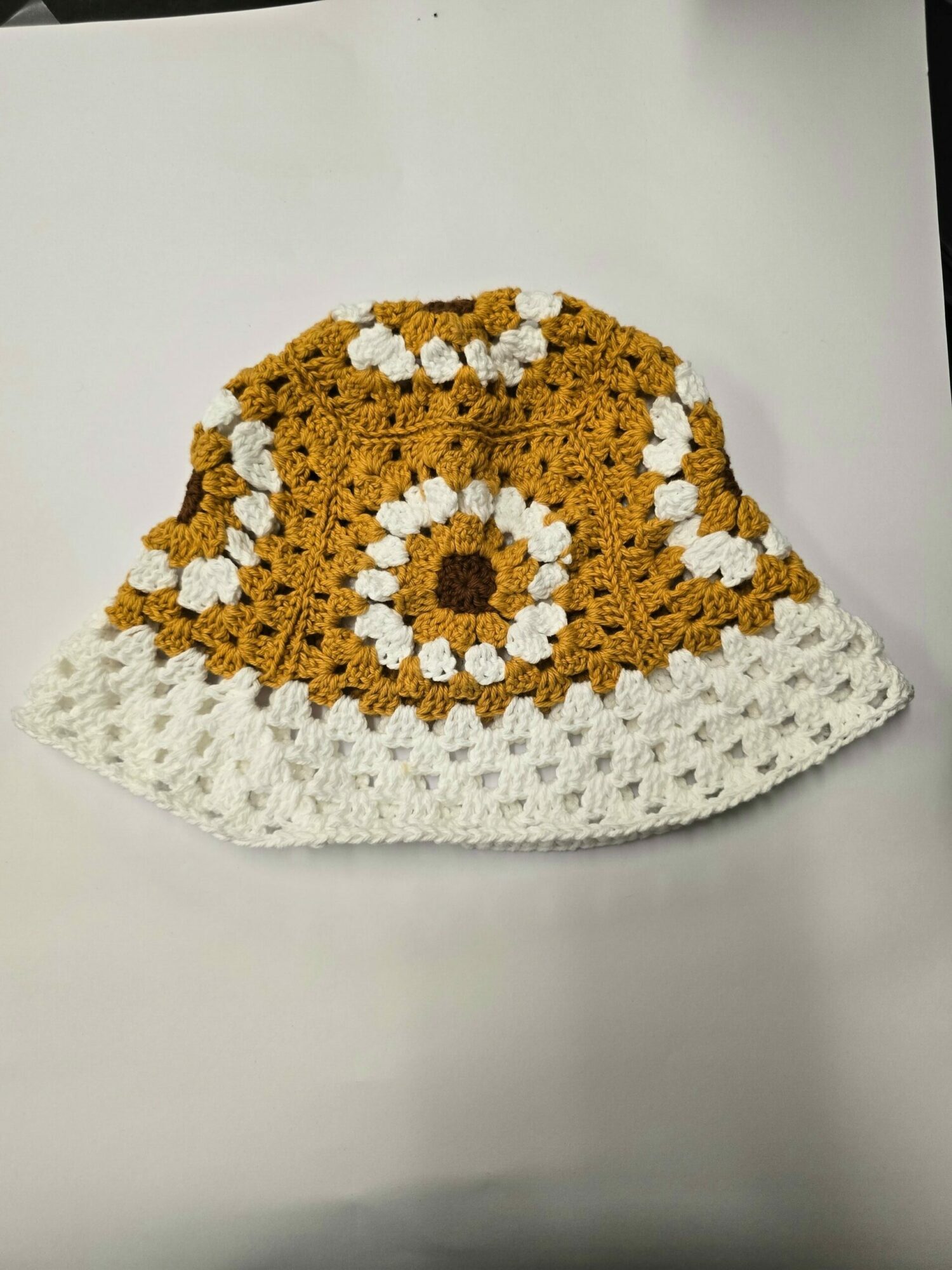 Crocheted half-circle piece with yellow, white, and brown colors, placed on a white surface.