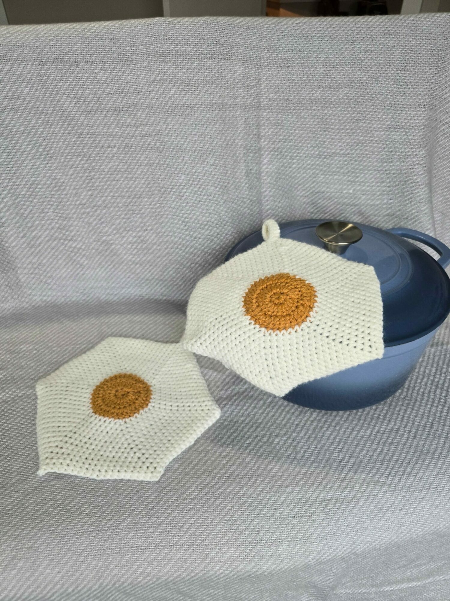 Two cloth face masks with brown circular designs, placed on a gray fabric surface with a blue bowl nearby.