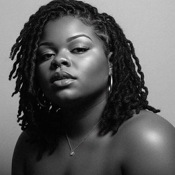 Portrait of a woman with natural hair, wearing hoop earrings and a necklace, looking confidently at the camera.