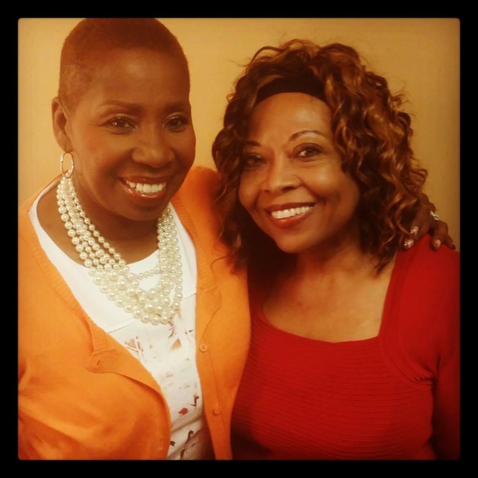 Two women smiling, one with short hair and pearl necklace, the other with curly hair and red top, close together.