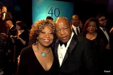 Two people dressed formally, smiling at a celebration event with a large blue sign in the background.