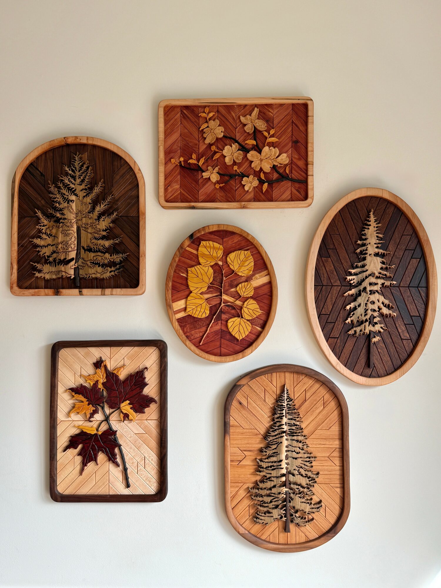 Six framed nature-themed artworks with trees and leaves on a light-colored wall.