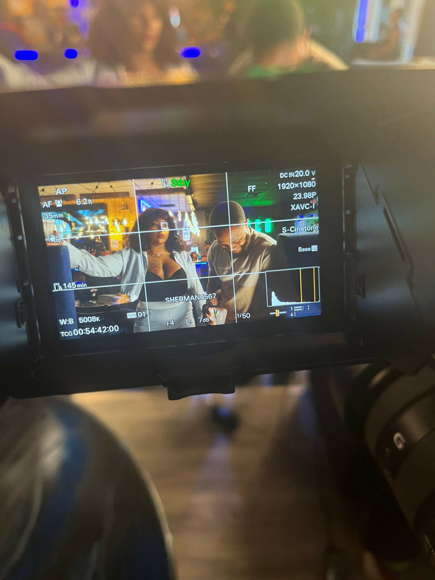 Camera screen showing two people sitting at a table in a lively indoor setting.