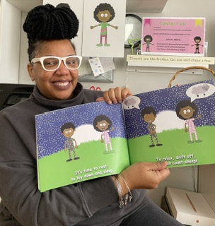 Person with glasses and braided hair holding a children's book with illustrations of children outdoors, smiling.