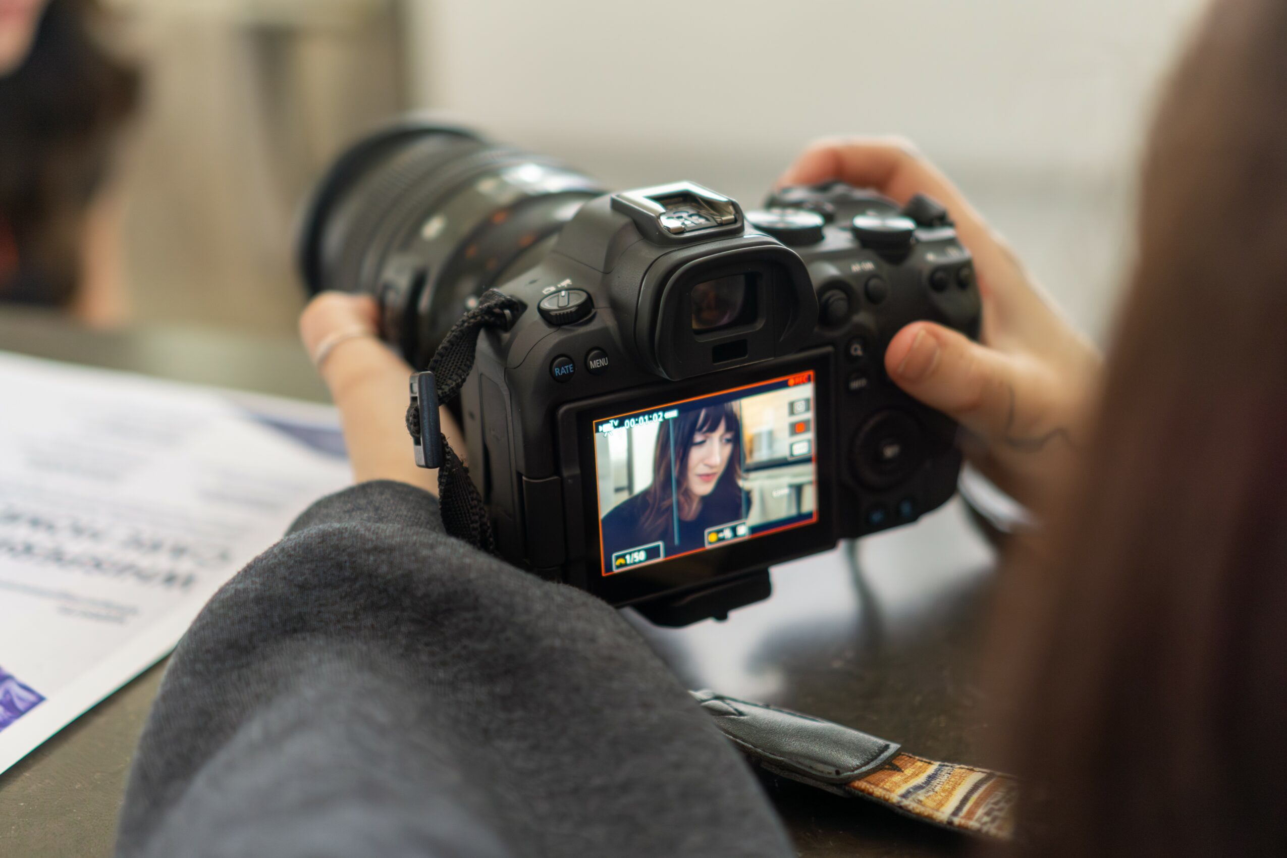 Person holding a camera, capturing a photo of a woman with glasses in a library or bookstore, with bookshelves in the background.
