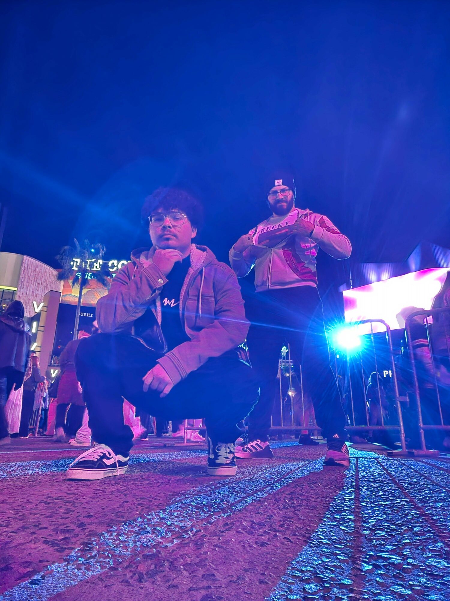 People sitting outdoors at night, with a bright blue light in the foreground, and a person standing in the background.