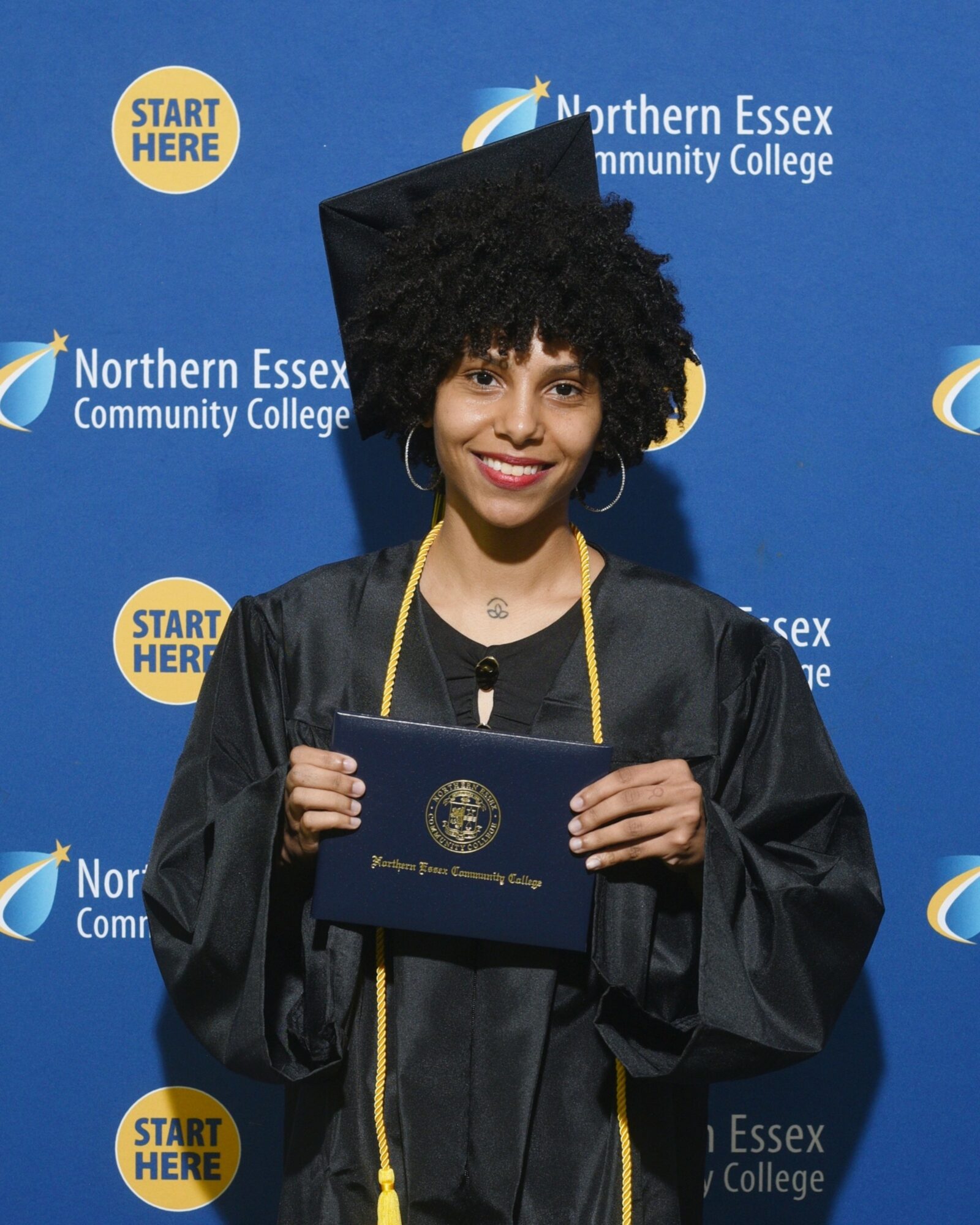 Young woman in graduation cap and gown holding diploma, smiling, against a blue background with college logos.