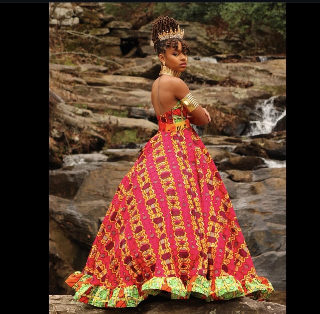 Woman in colorful dress standing by a rocky stream with water flowing over rocks.