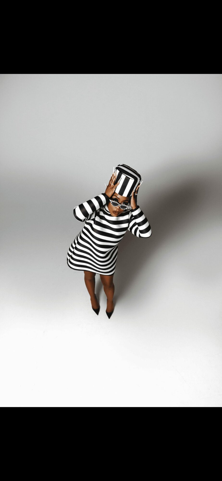 Person in striped dress holding a striped box over face, standing against a plain background.