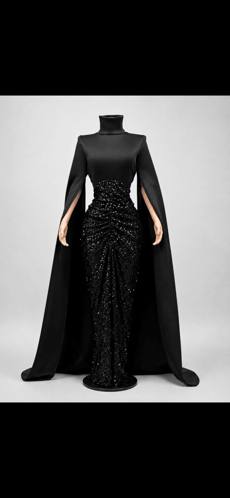 Black gown with a high neckline, long cape, and sequined skirt, displayed on a mannequin against a white background.