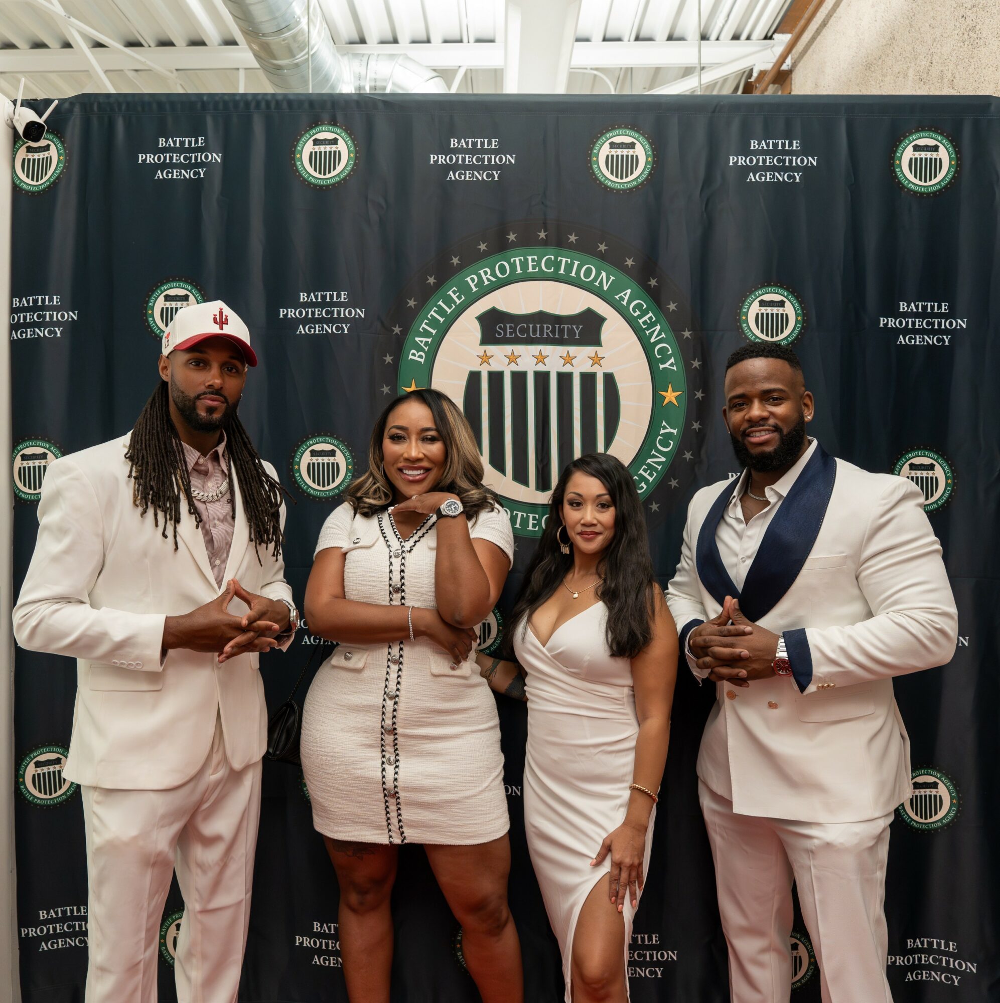 Four people standing in front of a backdrop with the Battle Protection Agency logo, smiling and dressed formally.