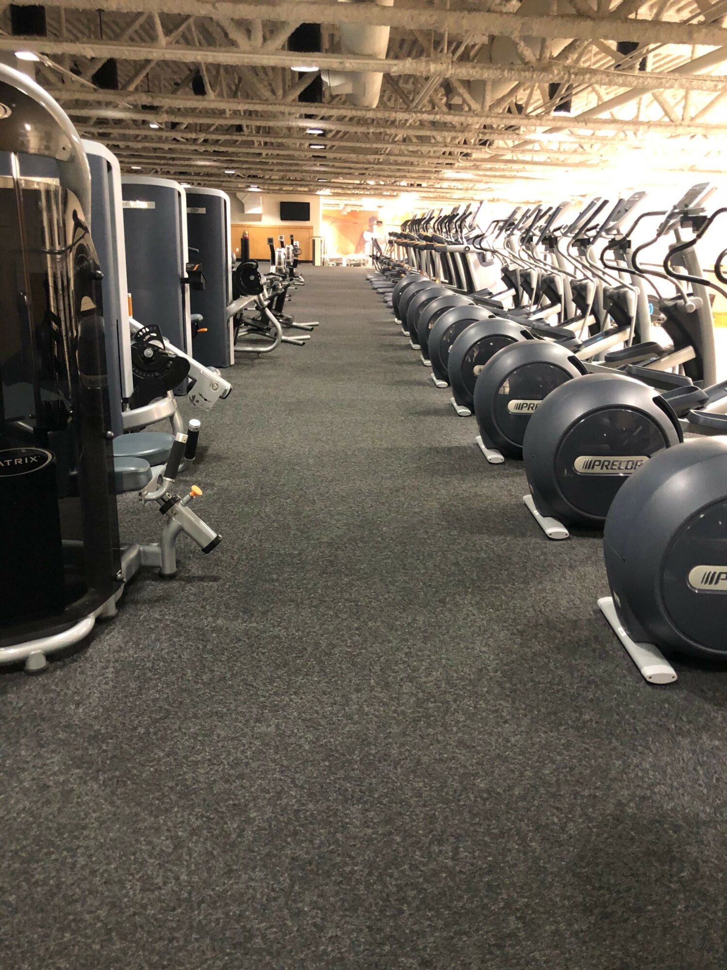 Gym with exercise bikes and equipment along a carpeted aisle, ceiling with exposed wooden beams.