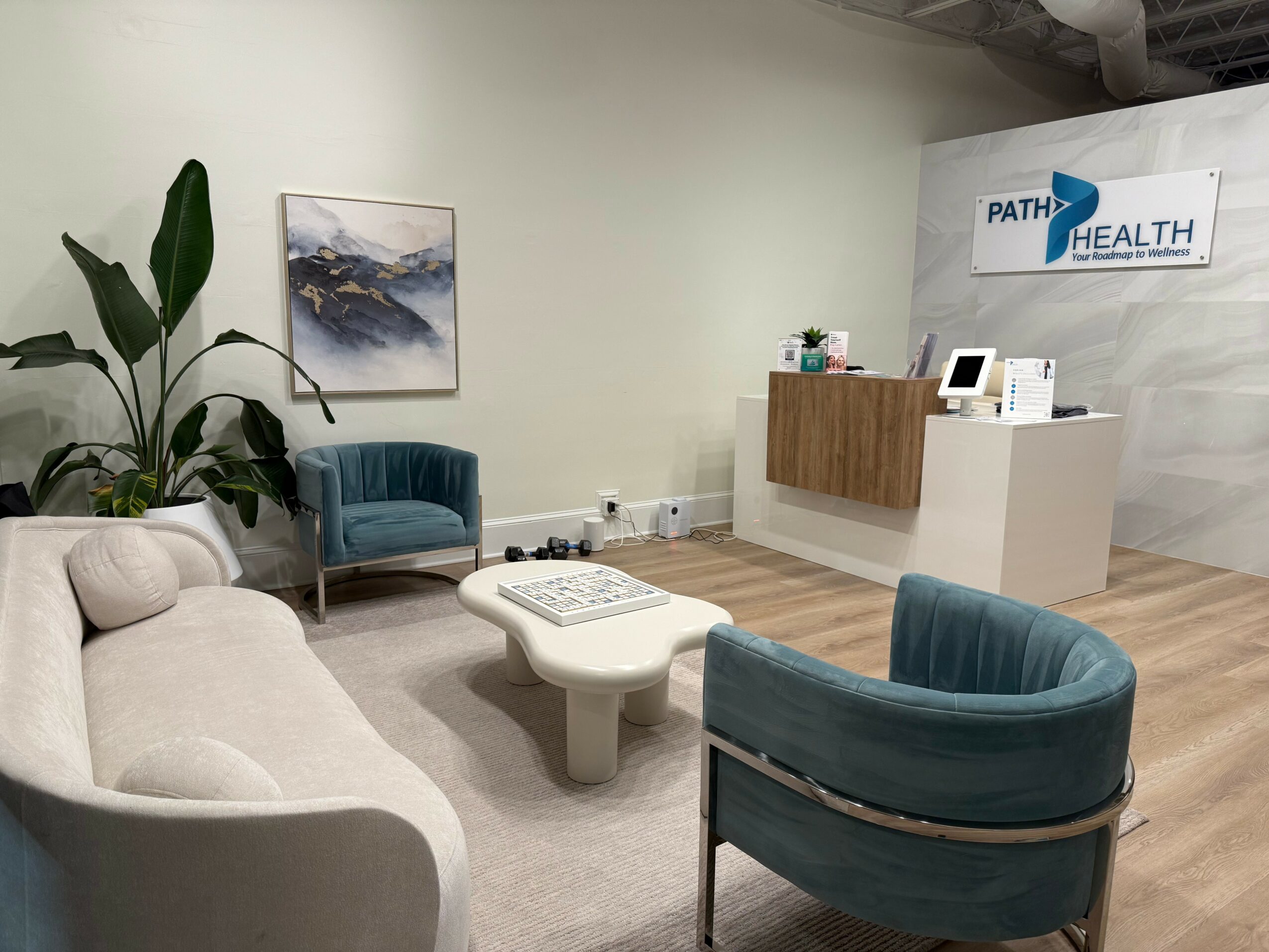 Waiting area with chairs, a coffee table, a plant, and a reception desk in a healthcare office.